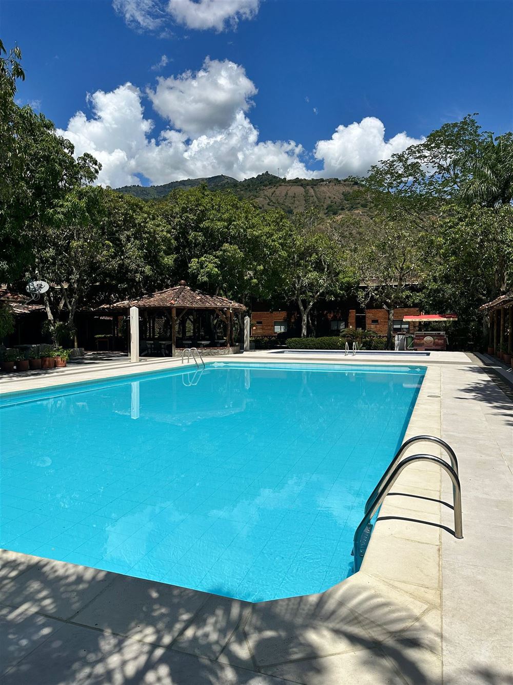 Piscina de adultos con agua azul, árboles alrededor y montañas al fondo