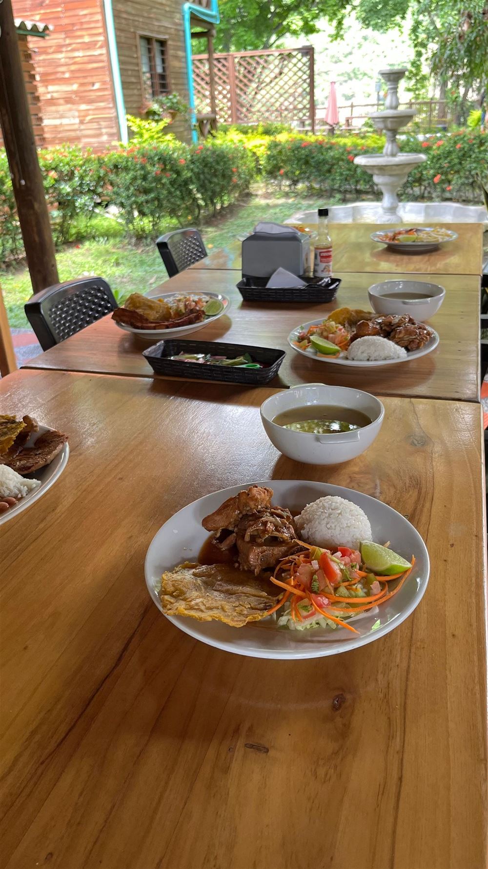 Platos servidos en una mesa de madera del restaurante, con jardín y fuente al fondo