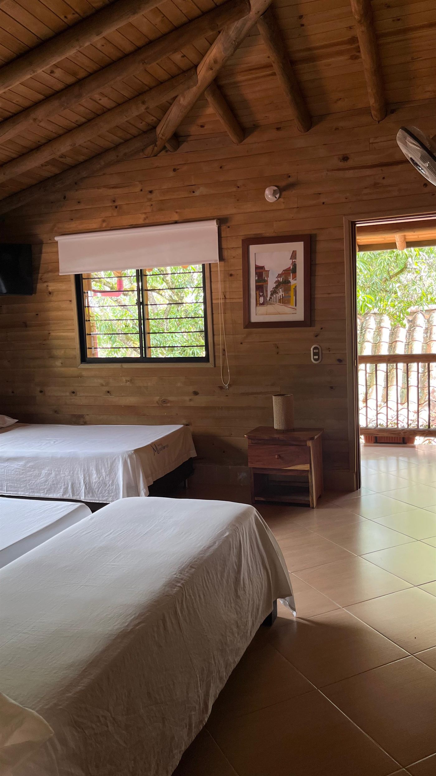 Habitación con aire y agua caliente: paredes y techo en madera, dos camas, televisor y salida al balcón