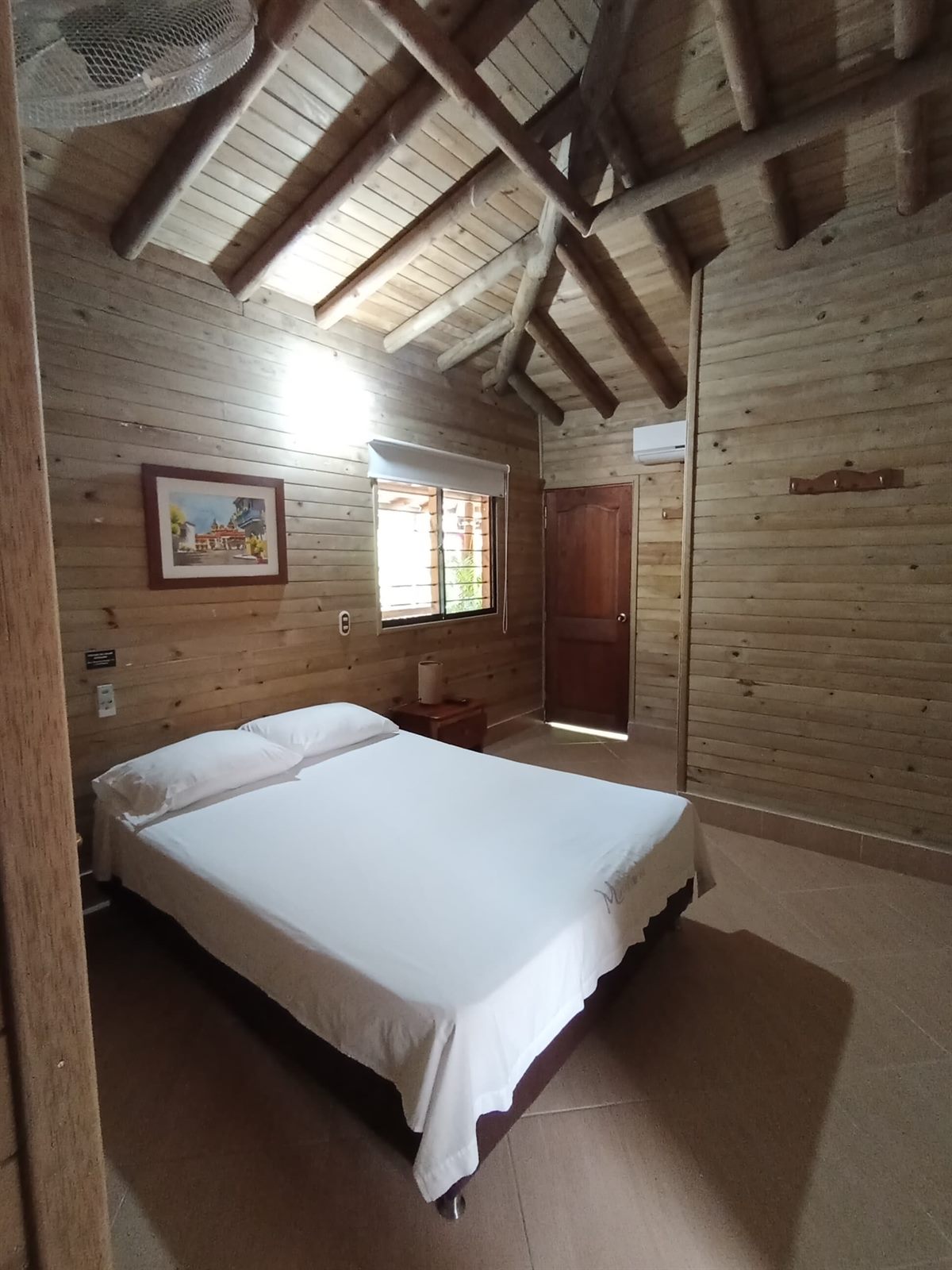 Habitación con aire y agua caliente con cama doble, ventana y paredes en madera