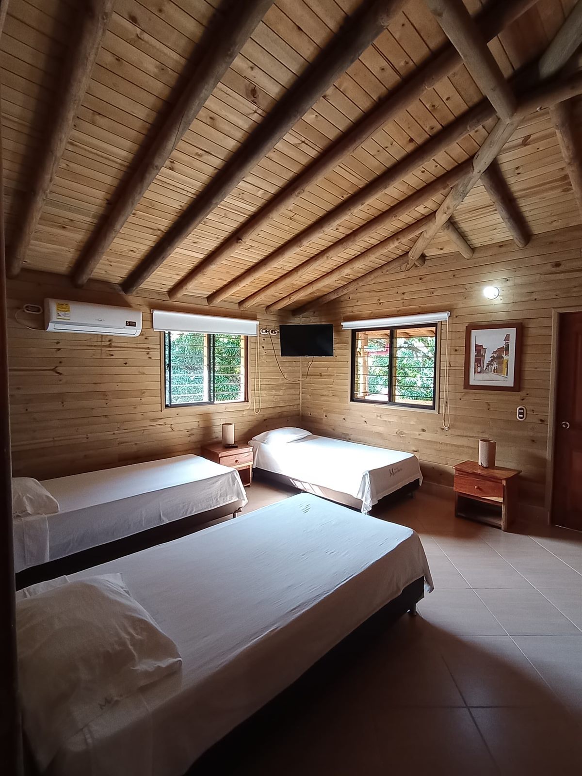 Habitación con aire y agua caliente: techo en madera, tres camas, aire acondicionado y televisor