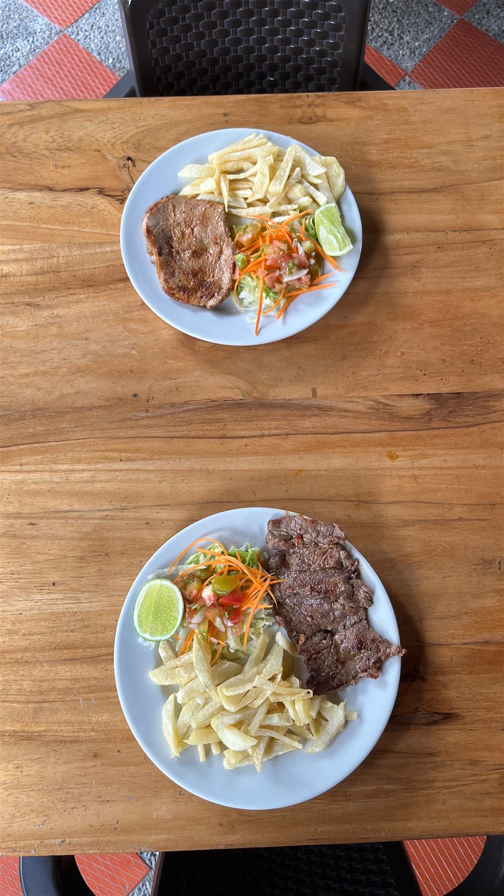 Carne asada con papas a la francesa, ensalada y limón, servida en una mesa de madera