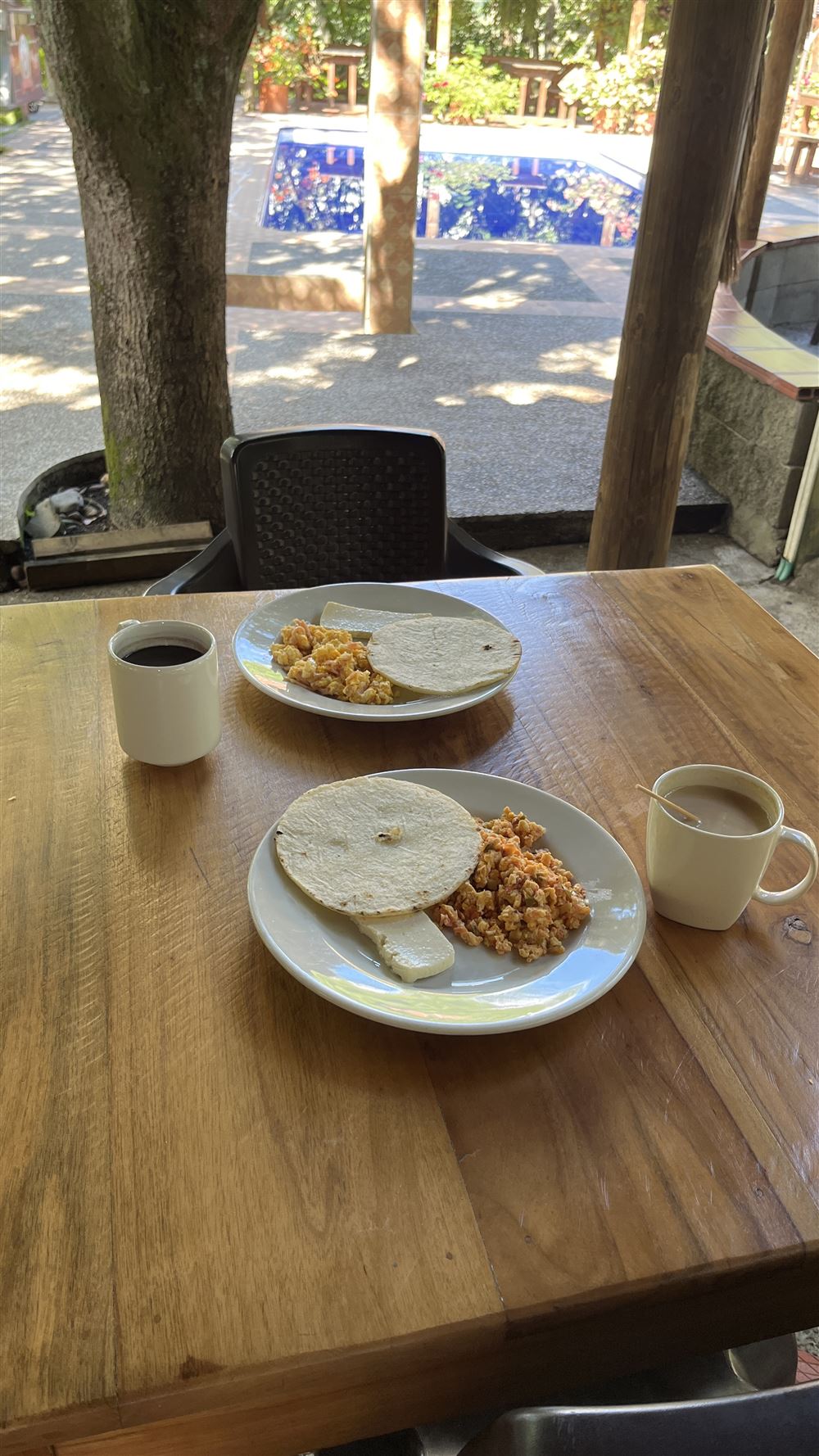 Desayuno con huevos pericos, arepa, quesito y café, con la piscina al fondo