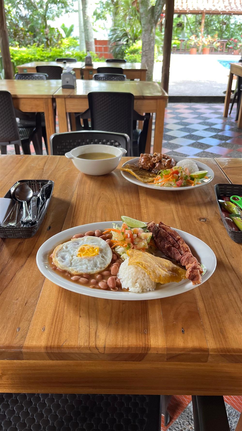 Bandeja de frijoles con chicharrón, huevo frito, arroz, arepa y ensalada, servida en una mesa de madera